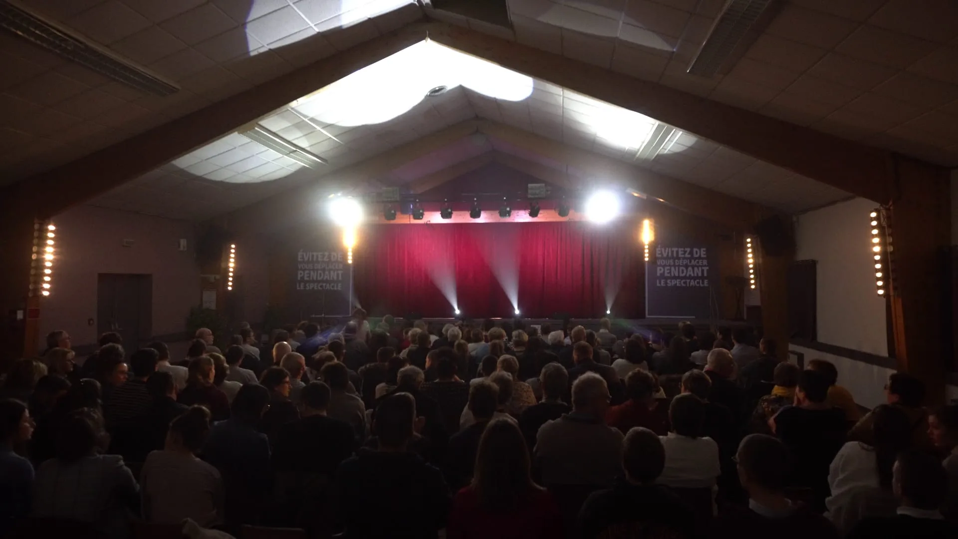 La salle pleine avant le début du spectacle, rideaux rouges et éclairage sur scène